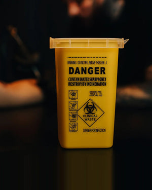 Yellow biohazard sharps container for clinical waste disposal – essential for safe tattoo studio hygiene and needle management.