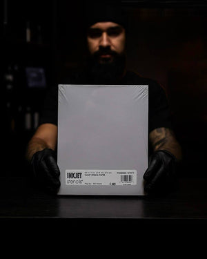 Tattoo artist holding pack of InkJet stencil paper sheets – professional-grade transfer paper from COZ Tattoo Supplies Canada.