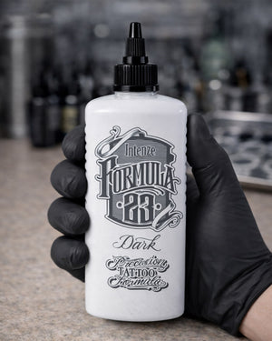 Intenze Formula 23 Dark tattoo ink bottle held in a tattoo artist’s gloved hand, professional studio photo, Coz Tattoo Supplies