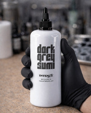 Intenze Light Grey Sumi tattoo ink 12 oz bottle held in a tattoo artist’s gloved hand, professional studio shot for Coz Tattoo Supplies