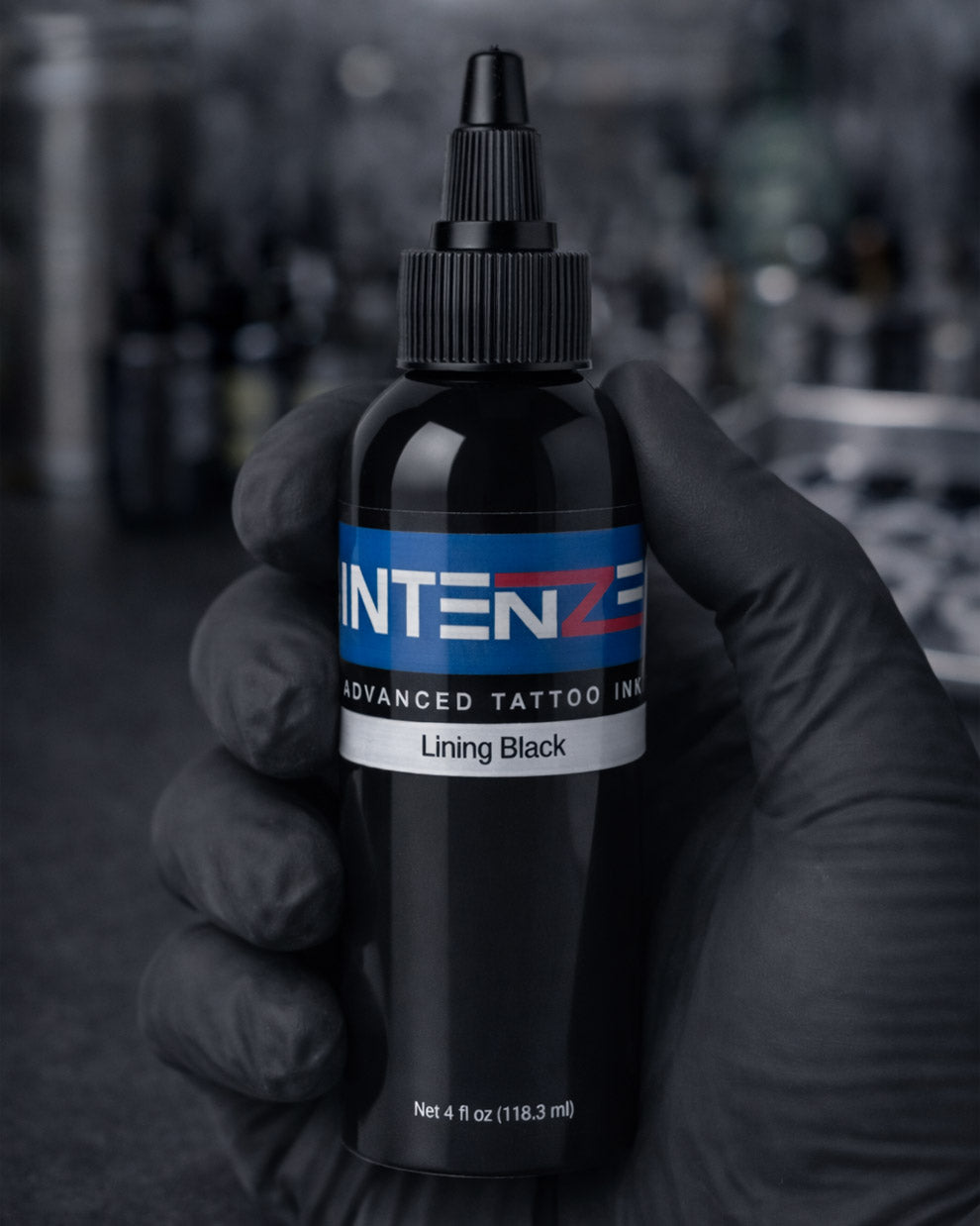 Intenze Lining Black 4oz tattoo ink held in a tattoo artist’s gloved hand, sharp label focus, professional studio lighting, Coz Tattoo Supplies