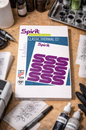 Spirit Thermal Paper 8.5×14 tattoo stencil paper box placed on a professional tattoo artist workstation with inks, tools, and stencil supplies