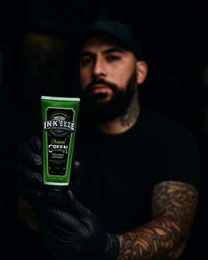 Tattoo artist holding INK-EEZE Green Tattoo Ointment 100ml Tube by COZ Tattoo Supplies Canada — vegan tattoo aftercare balm for professionals