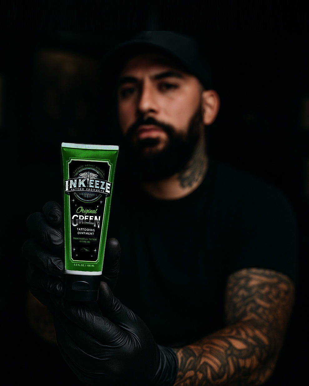 Tattoo artist holding INK-EEZE Green Tattoo Ointment 100ml Tube by COZ Tattoo Supplies Canada — vegan tattoo aftercare balm for professionals