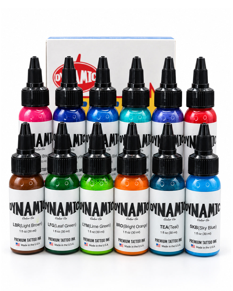 Twelve bottles of Dynamite Premium Tattoo Ink arranged in two rows in front of a branded box, showing a full range of colors including pink, blue, red, green, orange, and brown on a white background.