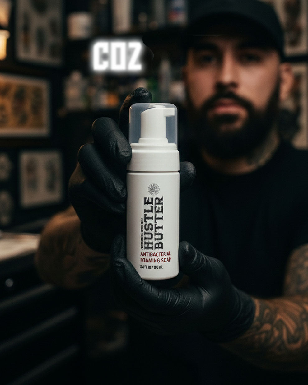 Hustle Butter Antibacterial Foaming Soap 7oz 207ml bottle held by tattoo artist wearing gloves in studio setting, professional tattoo cleansing soap used during tattoo sessions, available at COZ Tattoo Supplies