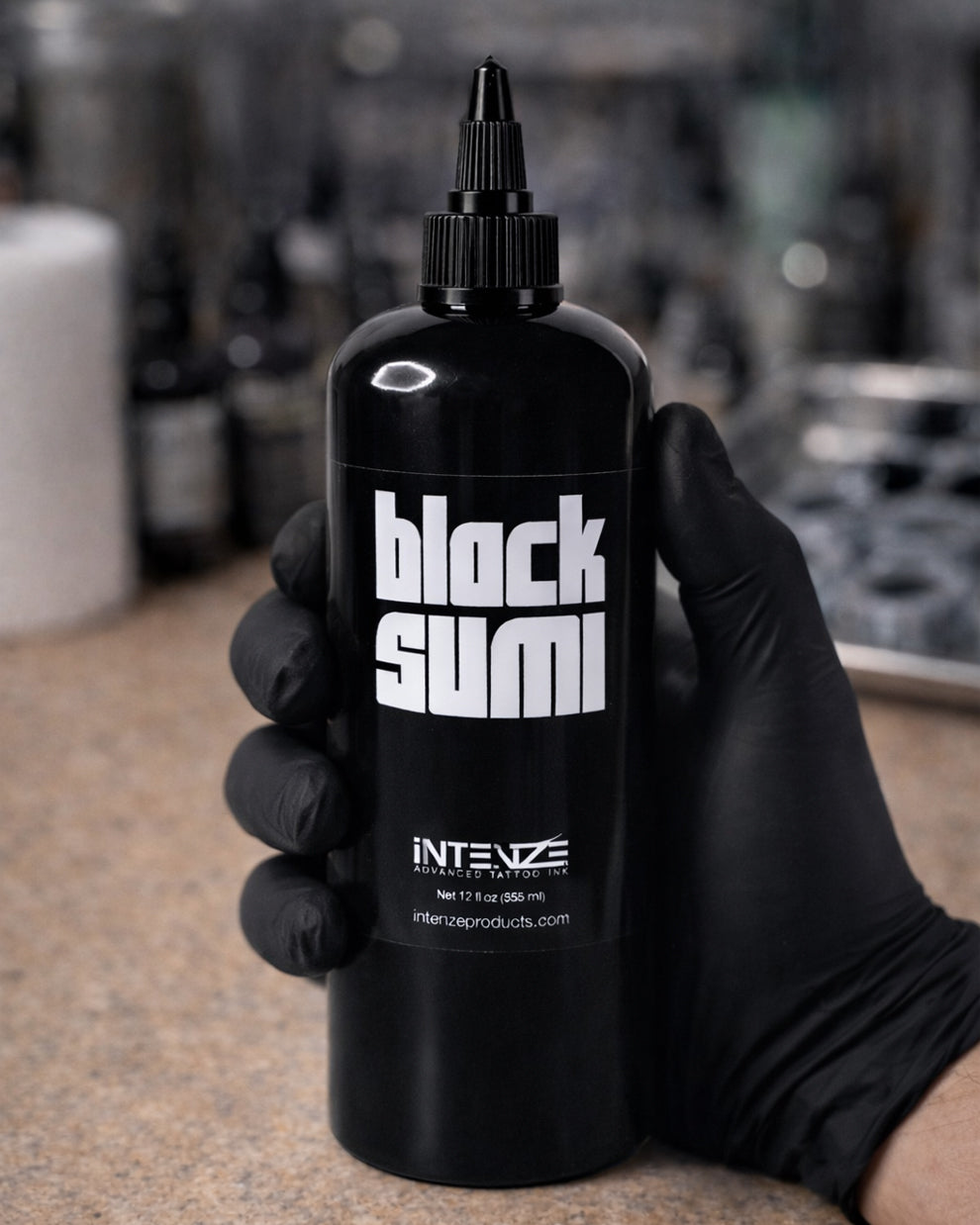 Intenze Black Sumi tattoo ink bottle held in a tattoo artist’s gloved hand on a neutral background, professional tattoo supply from COZ Tattoo Supplies
