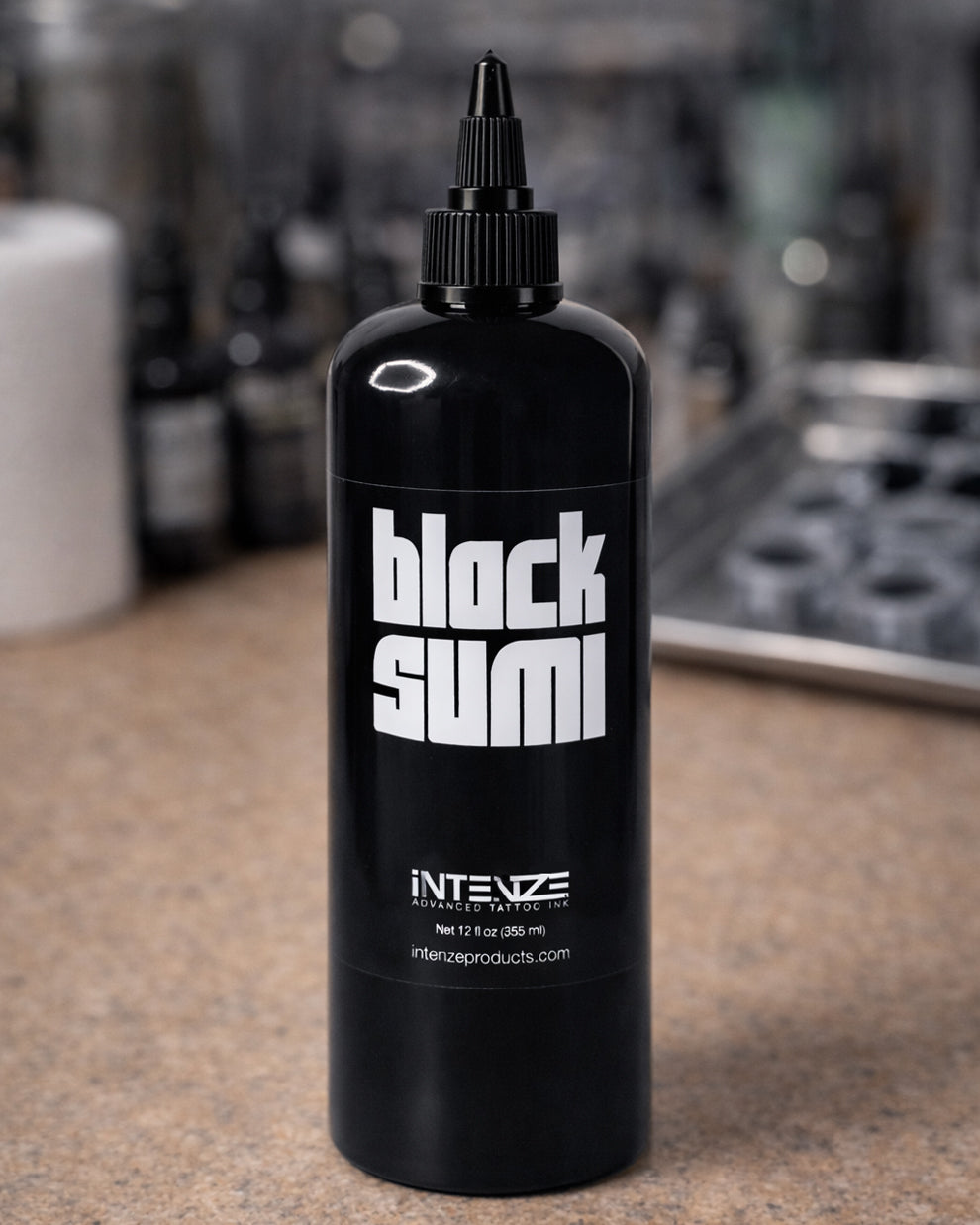 Intenze Black Sumi tattoo ink bottle placed on a tattoo artist workstation with professional tools, photographed for Coz Tattoo Supplies