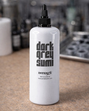 Intenze Dark Grey Sumi tattoo ink 12oz bottle on a tattoo artist workstation table, professional studio setup, Coz Tattoo Supplies