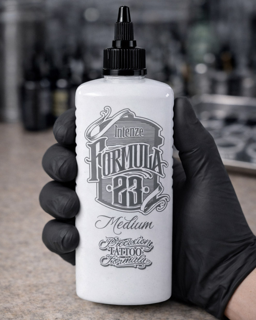 Intenze Formula 23 Medium tattoo ink bottle held in a tattoo artist’s gloved hand, clear label details, professional studio-style product photo