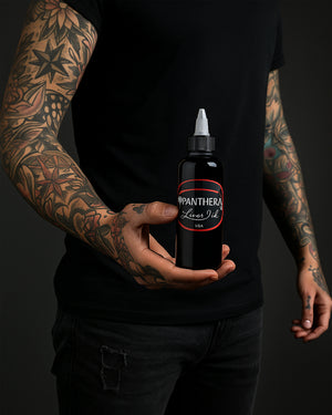 Tattoo artist holding Panthera Liner Dark Tattoo Ink 5oz bottle – trusted black ink for precise tattoo outlines.