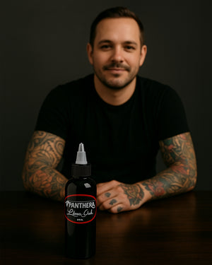 Panthera Liner Dark Tattoo Ink 5oz bottle on desk in front of tattoo artist – ideal black ink for clean, solid outlines.