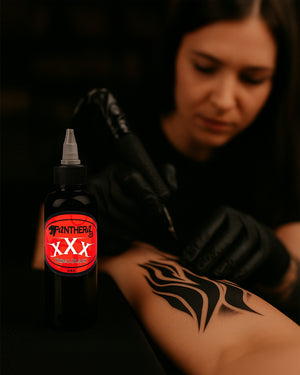 Tattoo artist using Panthera XXX Tribal Black Ink for bold tribal tattoo design on forearm.