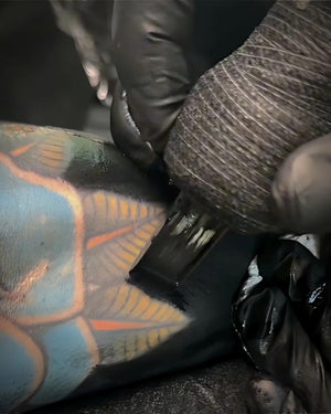 Tattoo artist applying solid black fill using Intenze Black Label Tattoo Ink during a session.